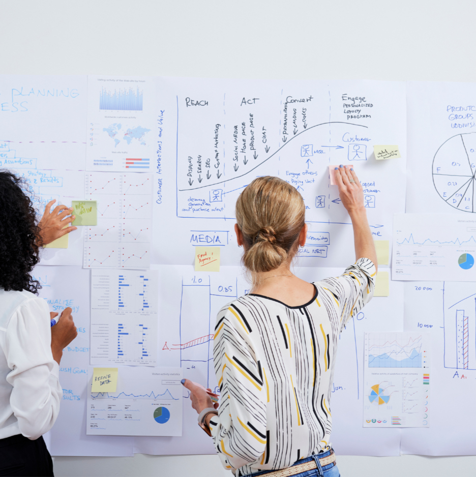 Two women working on a large whiteboard with diagrams and notes.