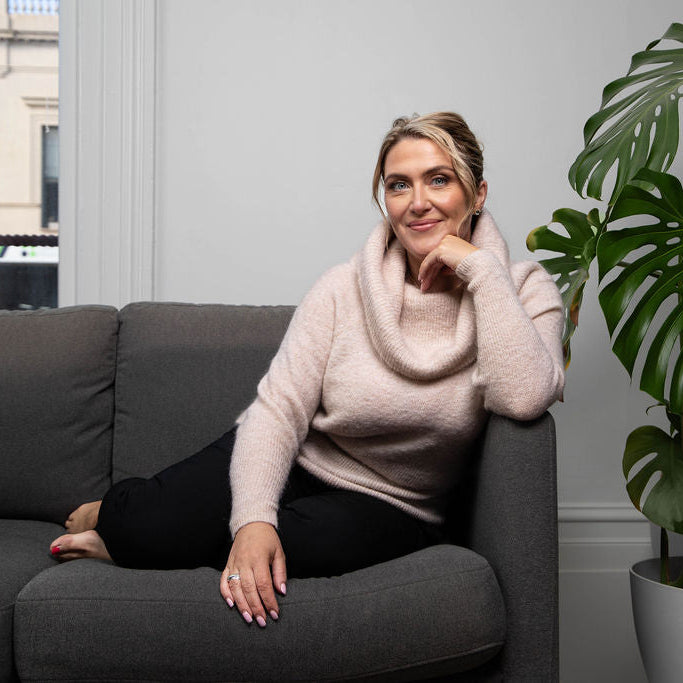 Woman sitting on a gray couch with a plant in the background