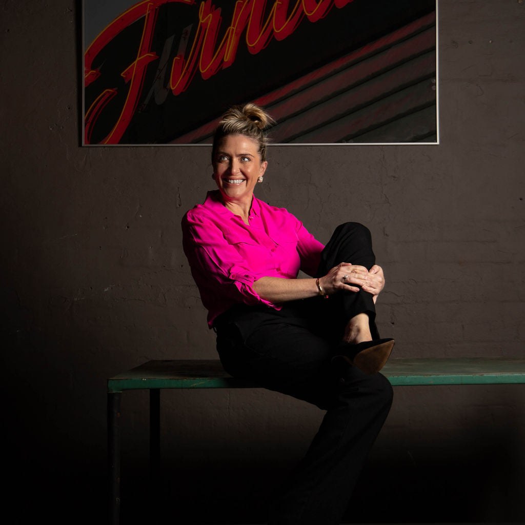 Felicity, The SheEO in a pink shirt sitting on a bench with a neon sign in the background