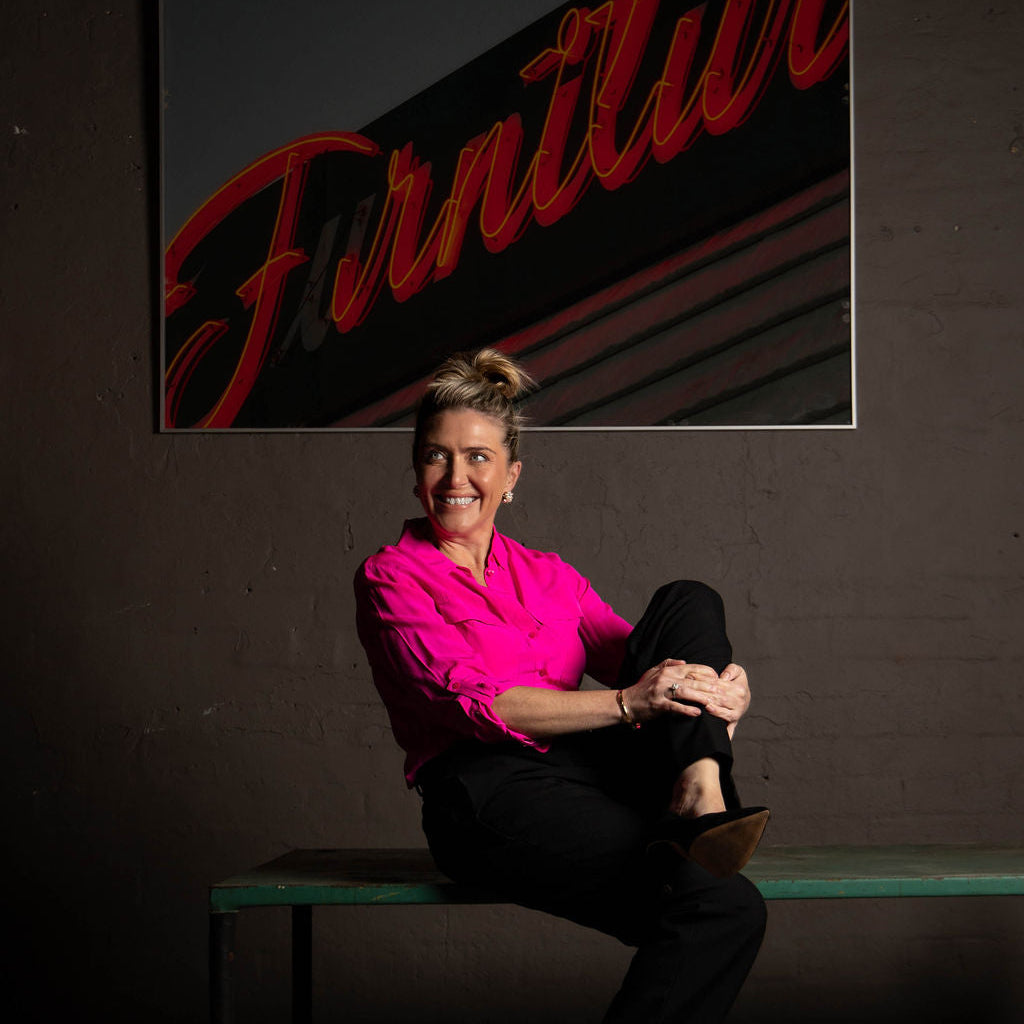 Felicity Pascoe in a pink shirt sitting on a bench with a neon sign in the background