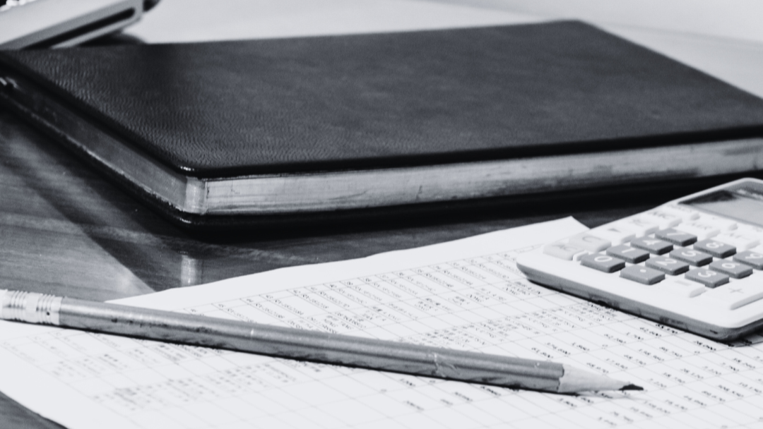 Notebook with pen, calculator, and closed laptop on a desk