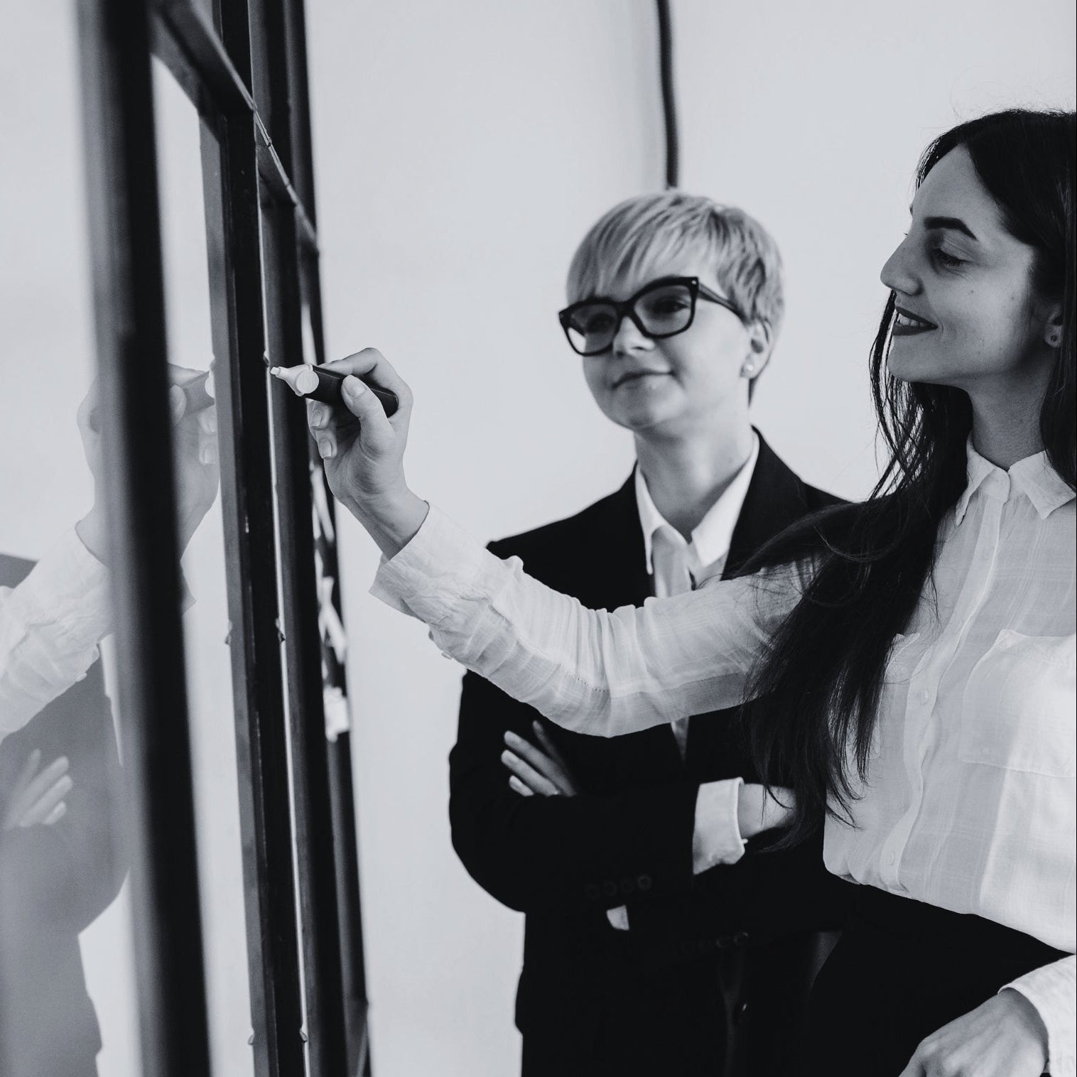Two women in business attire discussing something on a whiteboard.